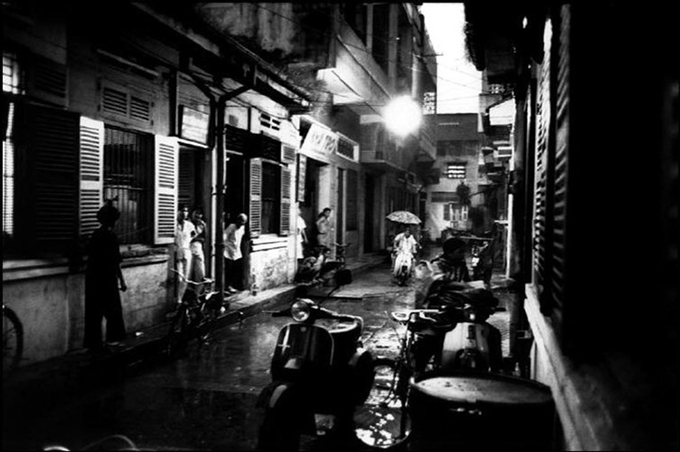 From doorways in an alley, people watch the rain.
