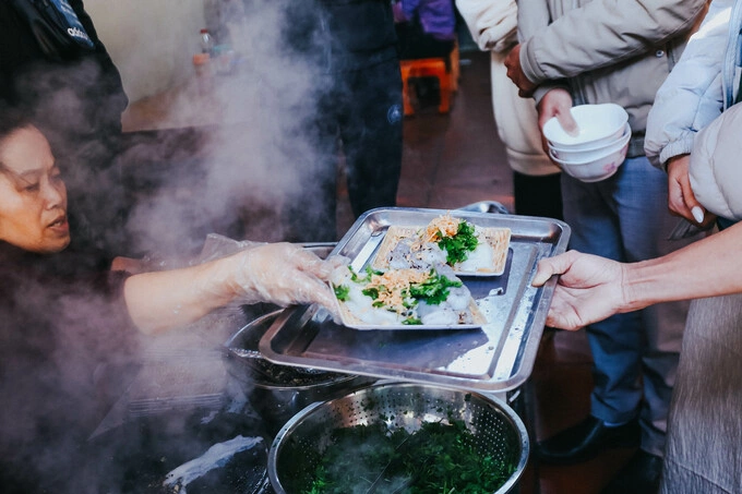 Bui Thai puts plates of rice rolls on a tray as her customers wait in line. Photo by VnExpress/Xuan Phuong