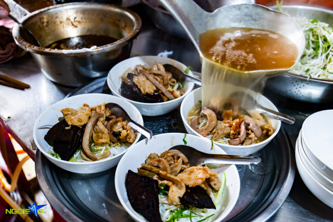 Broth is poured into bowls of pho with full toppings. Photo by VnExpress/Tung Dinh