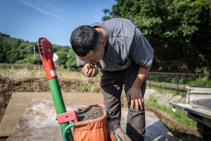This picture taken on June 13, 2023 shows Nobuyoshi Fujiwara, an owner of lettuce farm, smelling human feces-made fertilizer at his farm in Yokosuka city of Kanagawa prefecture. Photo by AFP/Yuichi Yamazaki