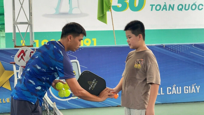 Ha Dung (R), 11, from Ba Dinh District, Hanoi, learning pickleball with his father under the guidance of a coach at a court in Cau Giay District. Photo by VnExpress/Thanh Nga