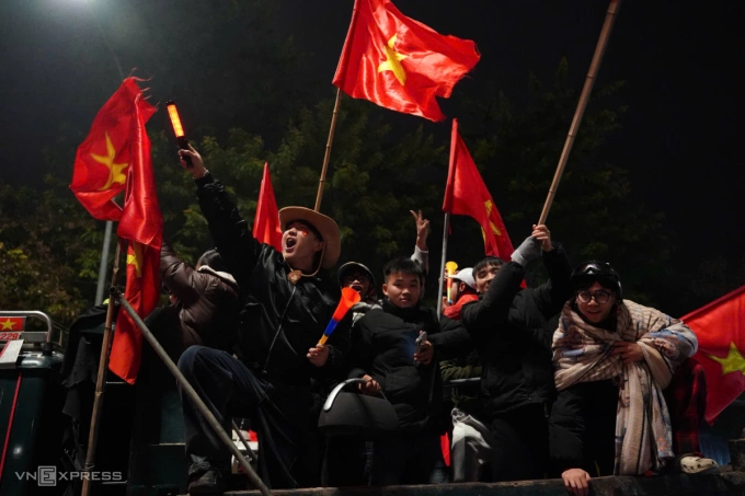 Un grupo de jóvenes aficionados en Hanoi agitan banderas y animan en la calle a las 2 de la madrugada.