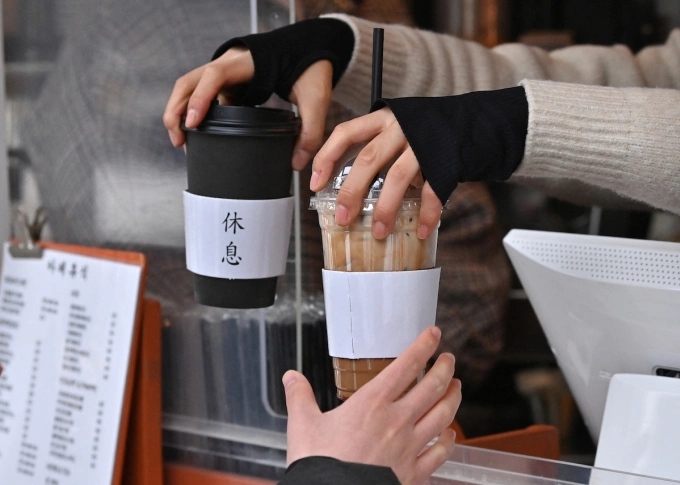 An employee passes out hot and cold coffee drinks to a customer at a cafe in Seoul, January 2023. Photo by AFP