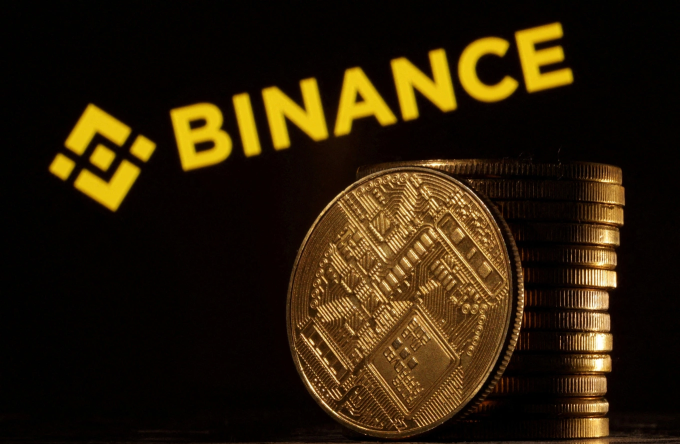 An illustration of crypto tokens seen in front of the logo of Binance. Photo by Reuters
