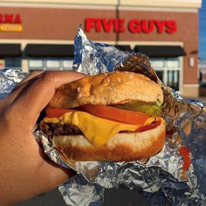 A person holds a burger outside of a Five Guys restaurant. Photo courtesy of Five Guys