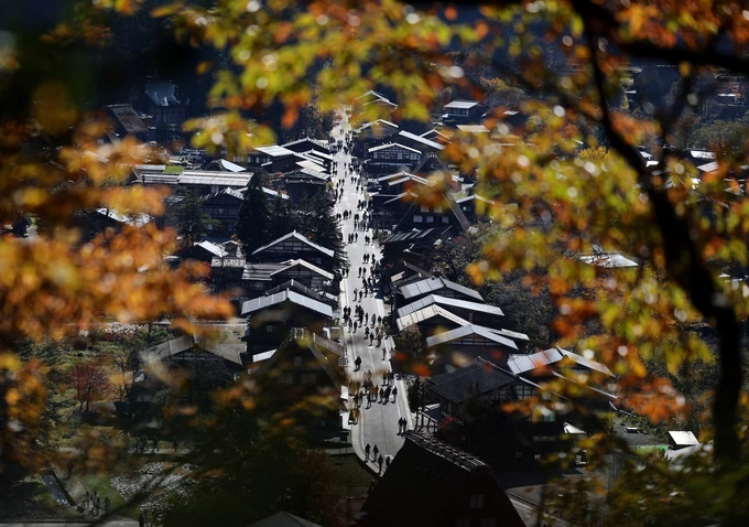 Visitors strolling next to traditional Gassho-style houses are seen through autumn-colored leaves at Shirakawa-go, a popular tourist spot and one of Japans UNESCO World Heritage sites, in Shirakawa village, Gifu Prefecture, Japan, November 15, 2025. Photo by Reuters