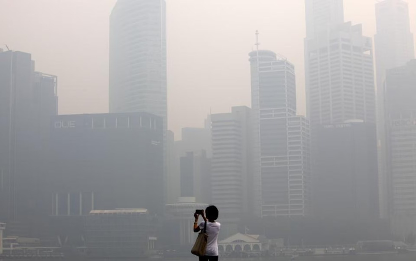 A woman takes photos of the hazy skyline of Singapore. Photo by Reuters