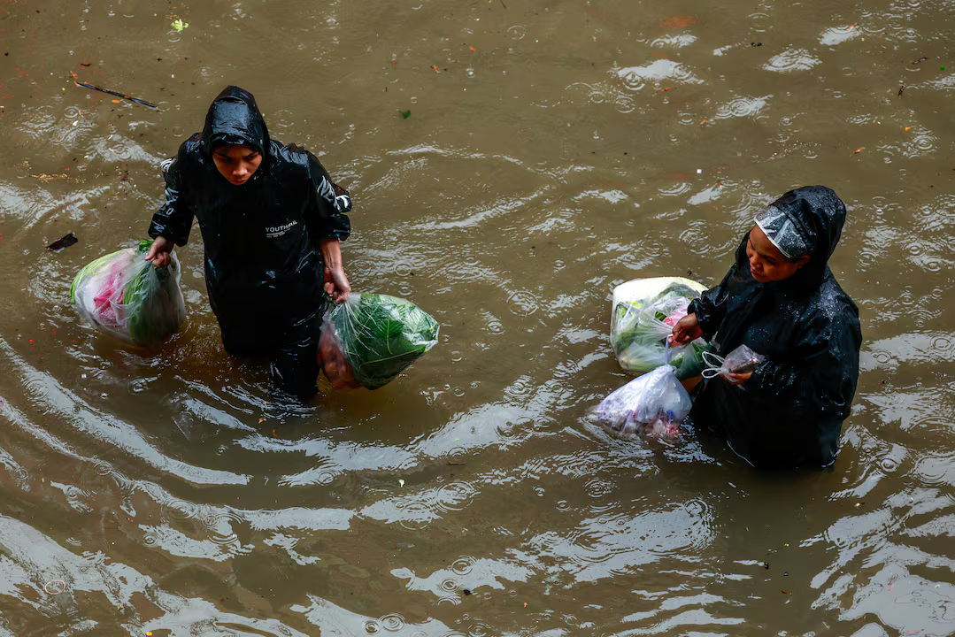 People carry groceries as they wade through a flooded street during heavy rain in Bangkok, Thailand, September 26, 2026. Photo by Reuters