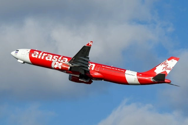 An AirAsia aircraft flies against a blue sky. Photo by Unsplash