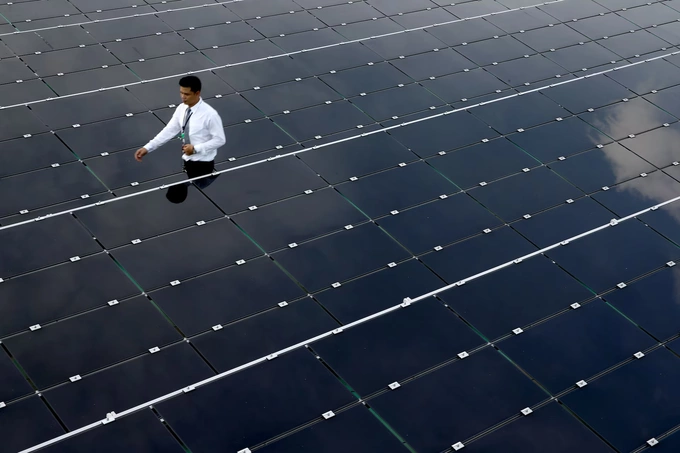 A man walks past solar panels on the roof of a building in Bangkok, Thailand, August 9, 2017. Photo by Reuters